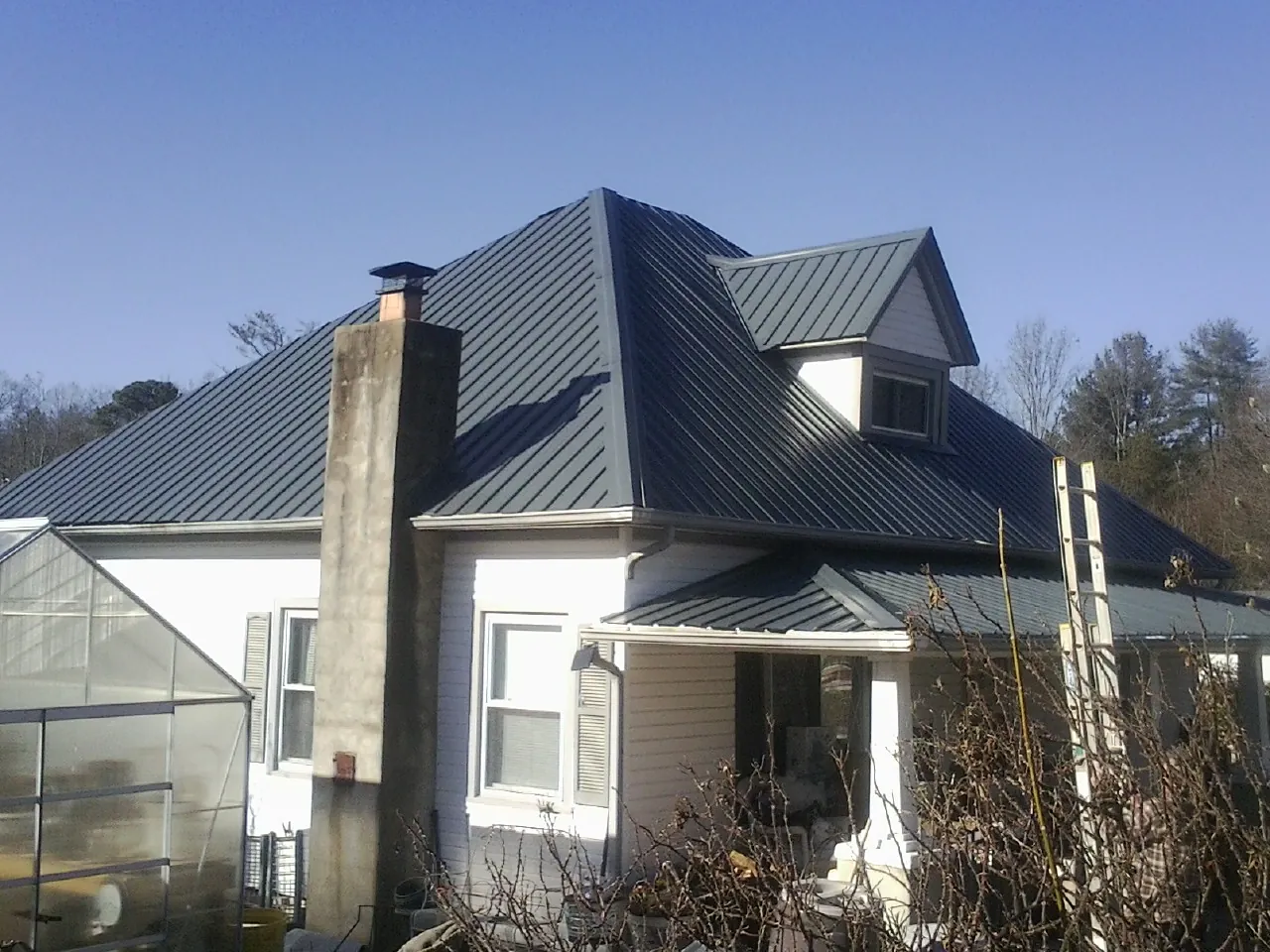 Dark blue standing seam metal roof on a white farmhouse with dormer — Slate & Tile Roof Repair by Roofing Brothers in South Milwaukee