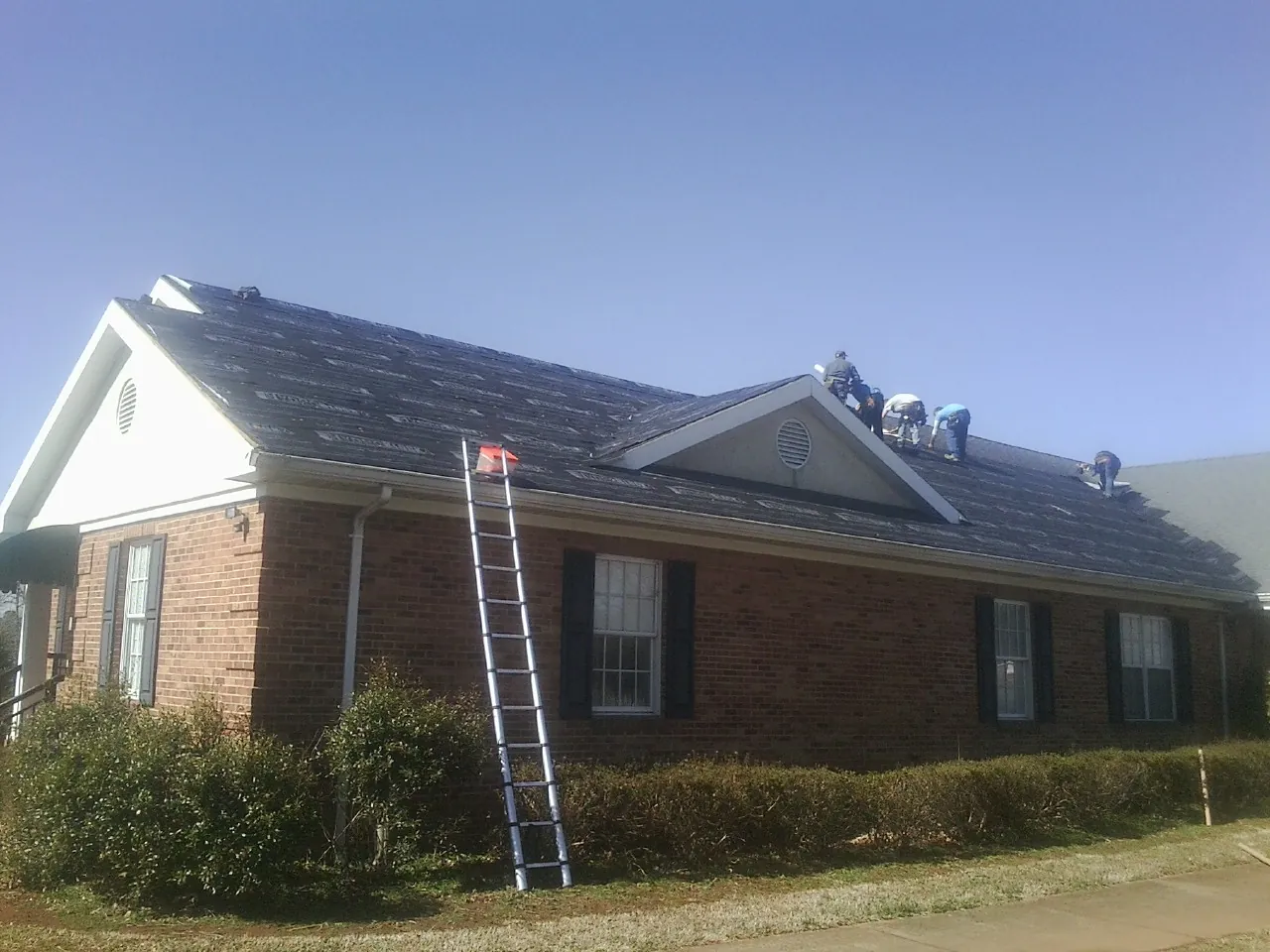 Crew tearing shingles off a brick ranch roof with a ladder set — Emergency Roof Repair work by our crew in South Milwaukee