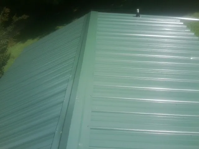 New green metal panels meeting at the ridge of a roof — Flat Roof Repair work by our crew in South Milwaukee