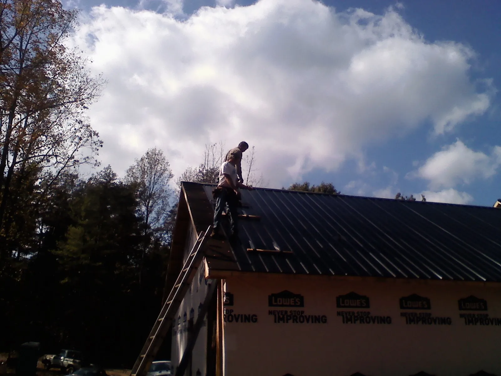Roofer fastening dark metal panels high against a cloudy sky, from a Roof Inspection job in South Milwaukee