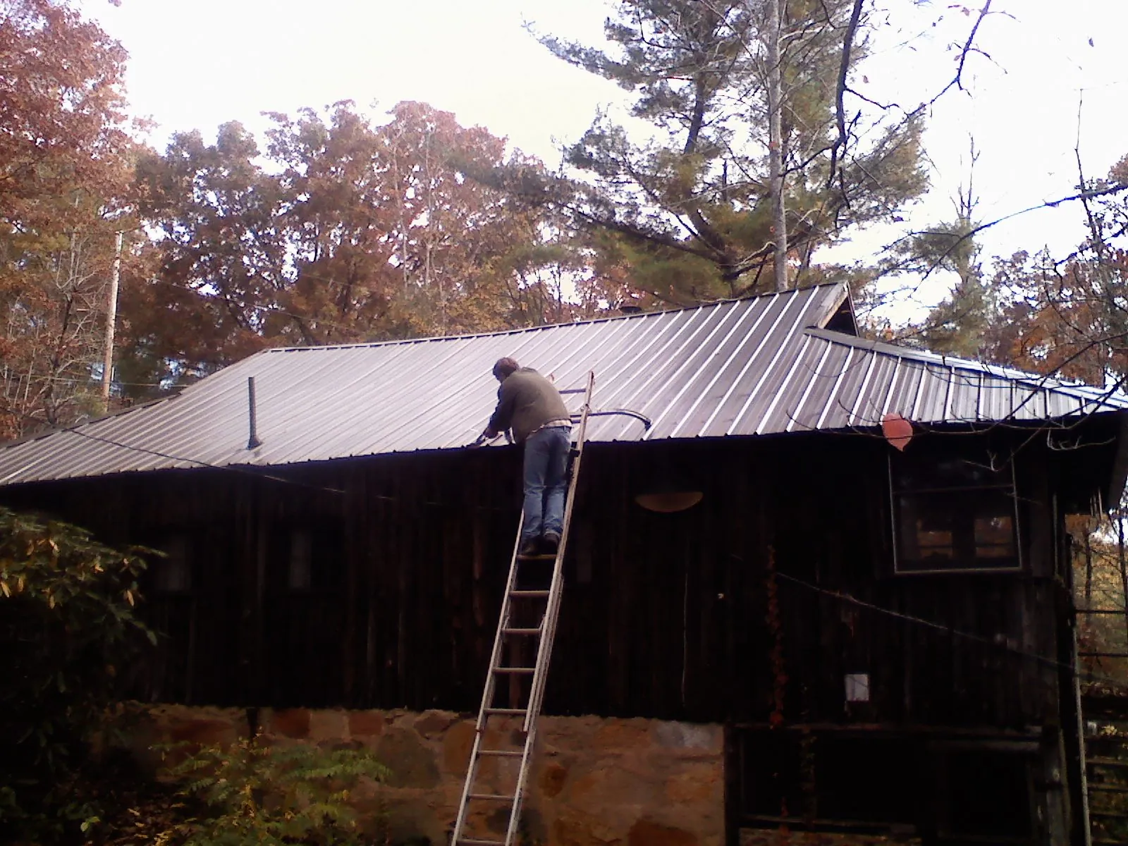 Roofer on a ladder working along the edge of a cabin metal roof in South Milwaukee