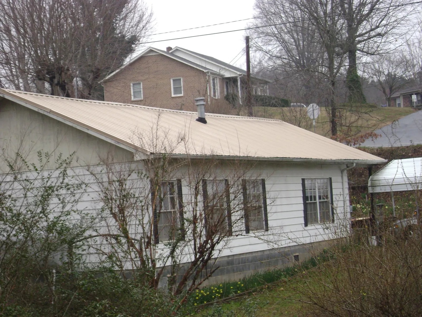 Tan metal roof on a white sided house set into a hillside — Commercial Roofing by Roofing Brothers in South Milwaukee
